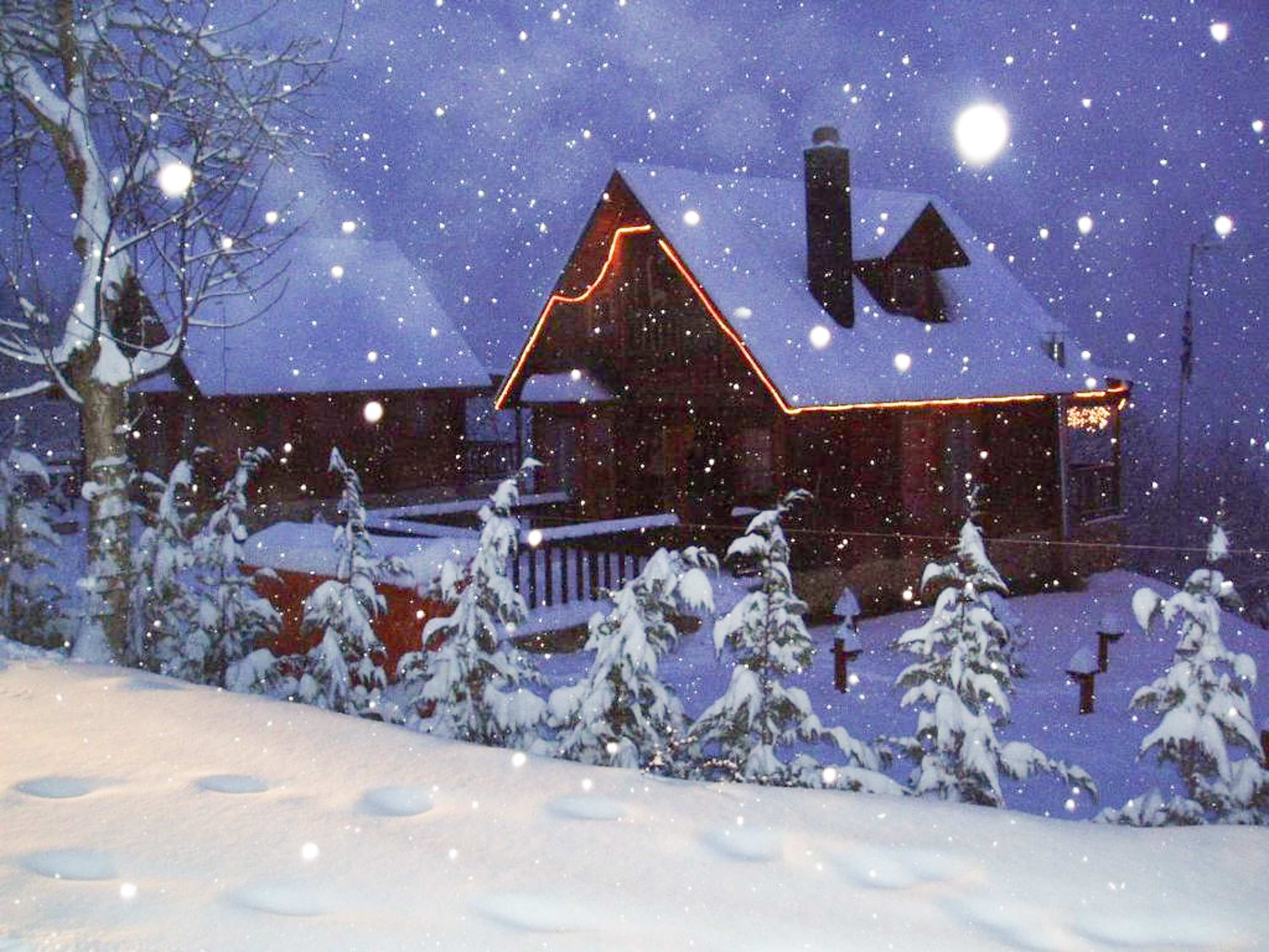 A snow-covered house with a lit roof and a visible chimney.