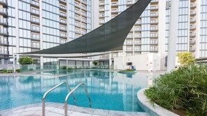Une piscine dotée d’un espace ombragé, entourée d’un immeuble de grande hauteur avec des balcons.
