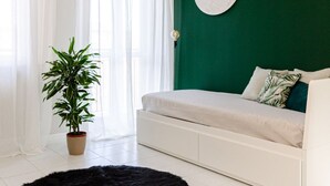 A bedroom with a green wall, a white bed, a potted plant, and a black rug. - VivimiHome | Cozy Design Flat - San Siro (Milano)