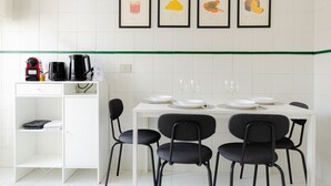 A modern kitchen with white cabinets, a white dining table set with four chairs, and four framed pictures on the wall. - VivimiHome | Cozy Design Flat - San Siro (Milano)