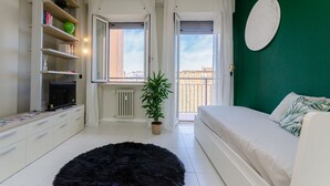 A bedroom with a bed, a black furry rug, a white sofa, a green plant, and a window with curtains. - VivimiHome | Cozy Design Flat - San Siro (Milano)