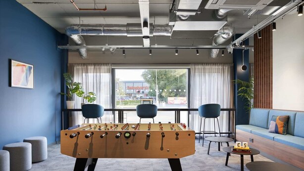 A modern room with a foosball table, two chairs, a sofa, and a view of a store through the window. - For Students Only Ensuites in Edinburgh (Edinburgh)