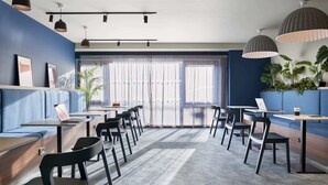 En moderne café med blå vægge, sorte stole og borde, store vinduer samt plantekasser.