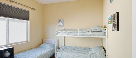 A dormitory room with two bunk beds, a ceiling fan, a window with blinds, and a small desk.