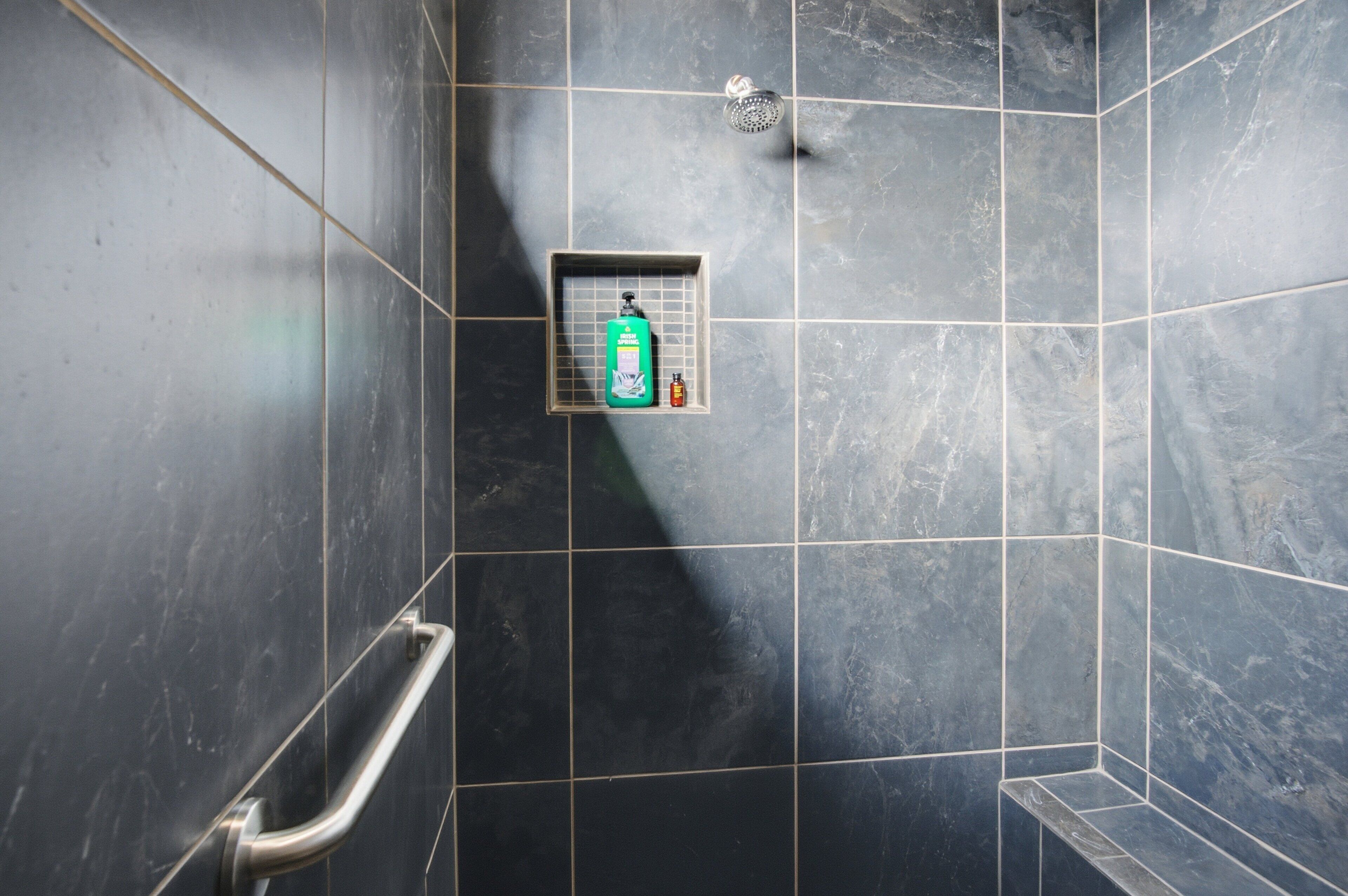 Un angolo doccia piastrellato con un mancorrente e uno scaffale con articoli da toilette.