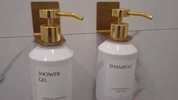 Two white bottles with gold pumps, labeled 'Shower Gel' and 'Shampoo', mounted on a marble wall.