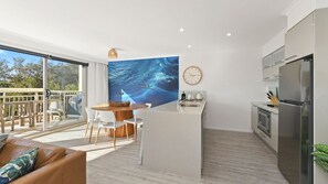 A modern kitchen with a large island, a dining area with a view, and a living space with a sofa. - Pacifico Flynn s beach 319 (Port Macquarie)