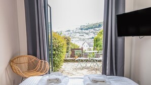 A hotel room with a bed, a wicker chair, and a view of a town through large windows. - Ty'r Ddraig (Dartmouth)