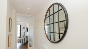 A hallway with a white radiator, a round mirror on the wall, and a striped sofa in the background. - Ty'r Ddraig (Dartmouth)