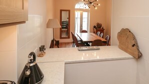 A modern kitchen with a central island, a dining area with a wooden table, and a large mirror reflecting the room. - Ty'r Ddraig (Dartmouth)