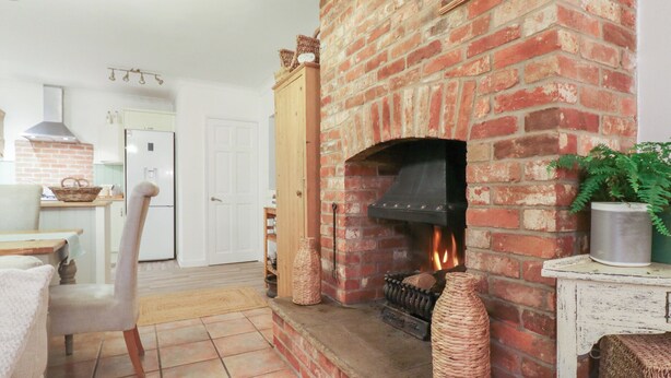 Ein gemütliches Wohnzimmer mit Kamin aus Backstein, einem Essbereich mit Tisch und Stühlen sowie einer Küche im Hintergrund.