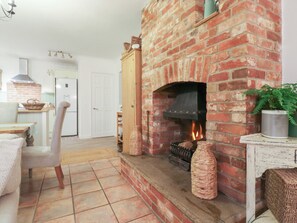 A cozy living room with a brick fireplace, a dining area with a table and chairs, and a kitchen in the background. - Berkley Cottage (Colchester)