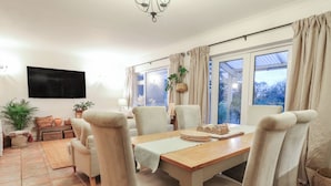 Ein Essbereich mit Holztisch, beigen Stühlen und einem an der Wand befestigten Fernseher.