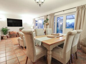 A dining area with a wooden table, beige chairs, and a TV mounted on the wall. - Berkley Cottage (Colchester)