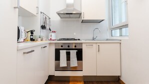 Une cuisine moderne avec des armoires blanches, une hotte de cuisinière en acier inoxydable, un four encastré et une fenêtre laissant entrer la lumière naturelle.