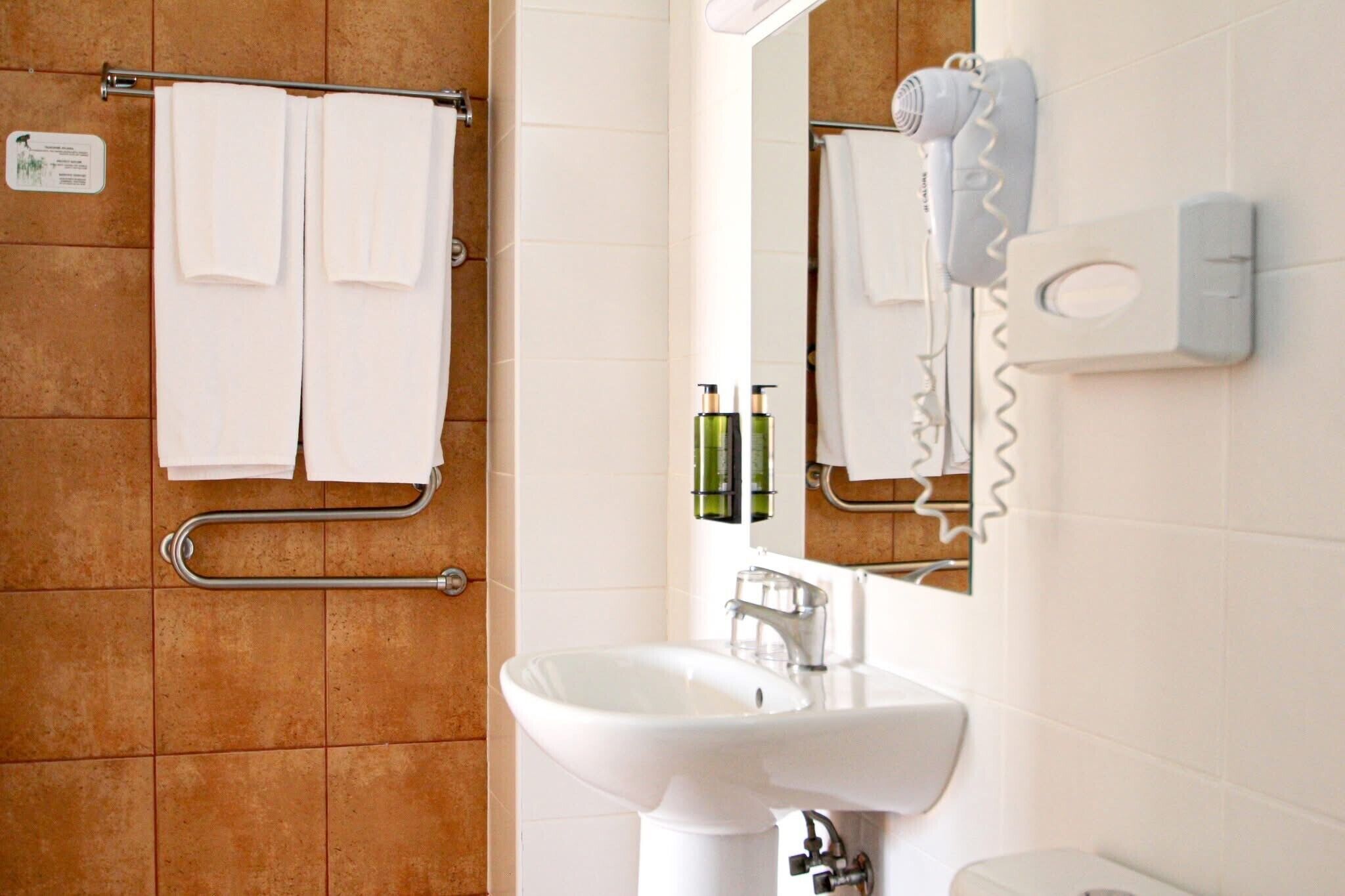 A bathroom with a white sink, a towel rack with two towels, a hairdryer, and a soap dispenser.