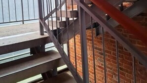 Un escalier avec des rampes en métal et des marches en bois, menant à un espace extérieur offrant une vue sur la mer.