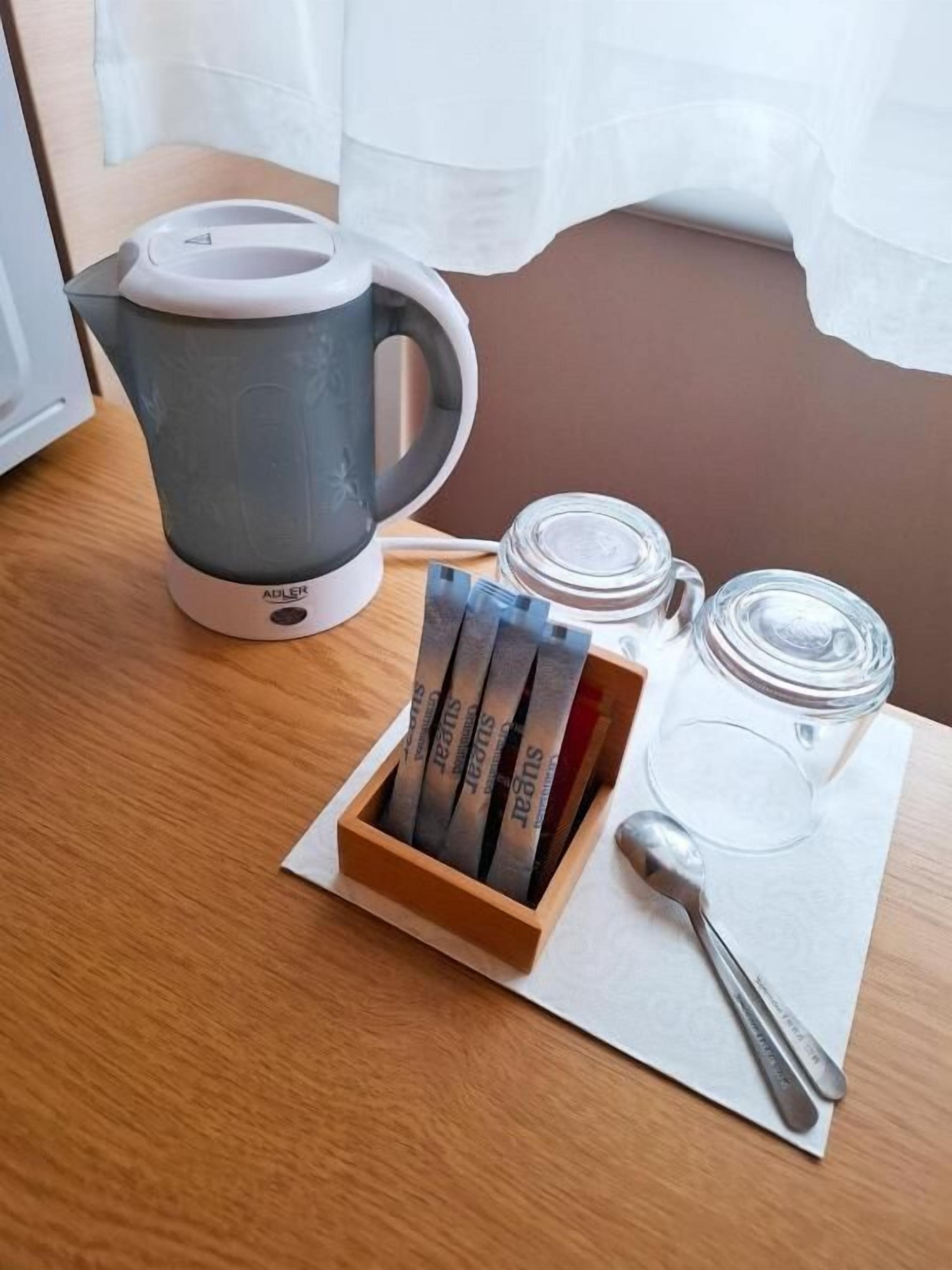 A coffee maker, sugar packets, a glass jar, and a spoon on a table.