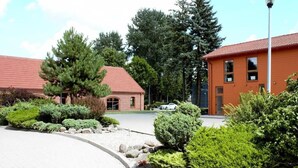 Un bâtiment avec un toit rouge et des murs en briques, entouré d’un aménagement paysager bien entretenu et d’une allée pavée.