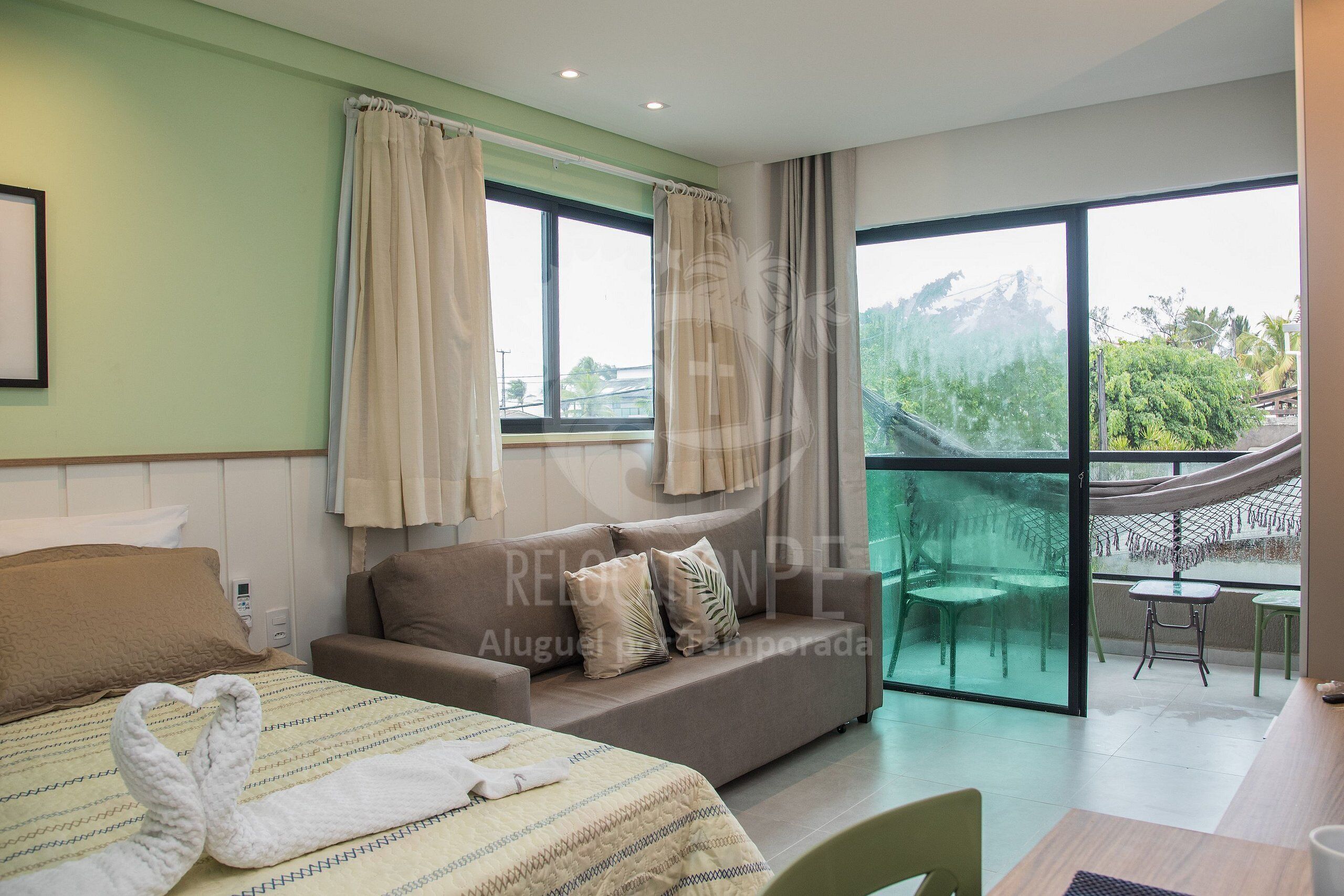 A hotel room with a bed, a sofa, a dining table, and a balcony with a view.