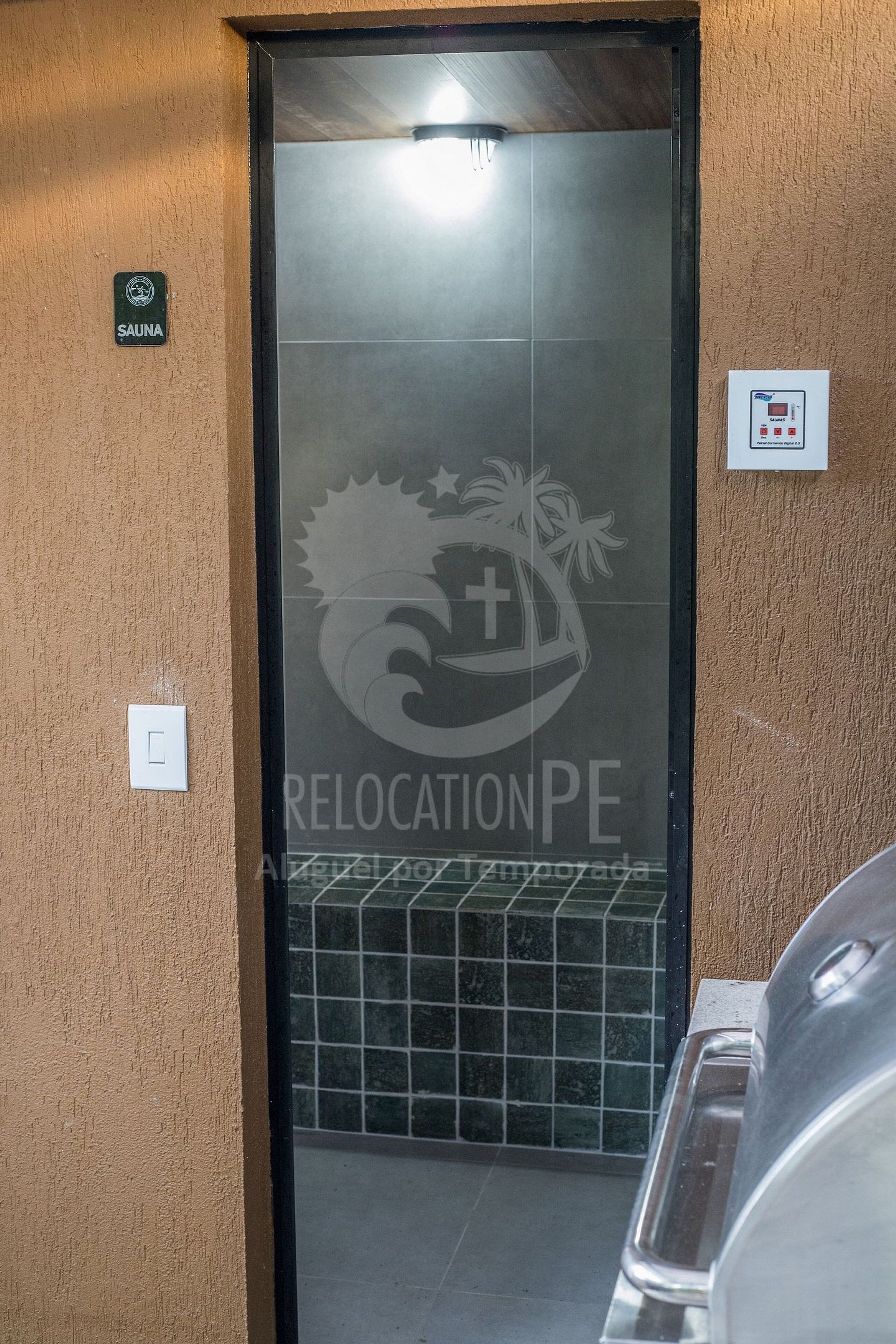 A sauna door with a logo, a control panel, and a tiled floor.