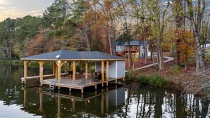 Eine Holzsteg, der sich in einen See erstreckt, mit einer überdachten Sitzgelegenheit und einem Haus im Hintergrund.