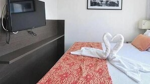 A hotel room with a flat-screen TV mounted on the wall, a bed with a red floral bedspread, and a neatly folded towel on the bed. - Condomínio Beach Class Conselheiro  (Ipojuca)