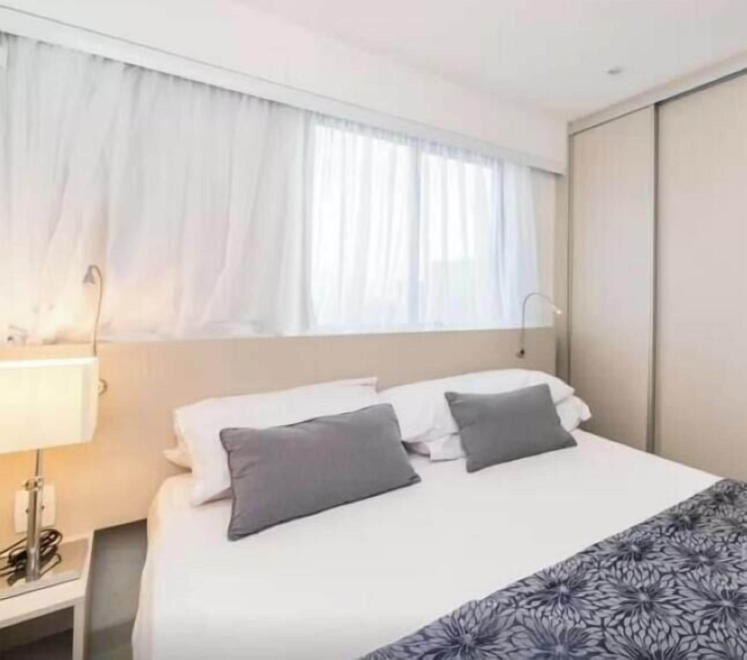 A hotel room with a bed, a nightstand, a lamp, and a window with curtains.