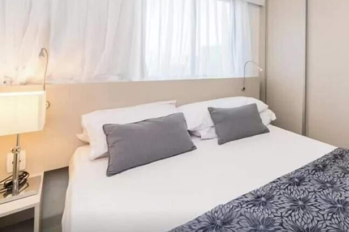 Une chambre d’hôtel avec un lit, une table de chevet, une lampe et une fenêtre avec des rideaux.