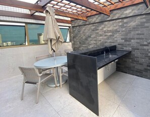 A patio with a table and chairs, a black countertop with a sink, and a brick wall. - Condomínio Beach Class Conselheiro  (Ipojuca)