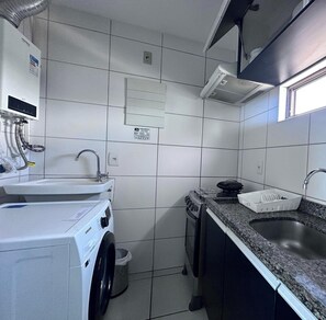 A compact kitchen with a washing machine, a sink, and a stove. - Condomínio Beach Class Conselheiro  (Ipojuca)