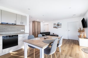 Una cocina moderna con electrodomésticos integrados, un comedor con mesa y sillas de madera, y una sala de estar con sofá y televisor.