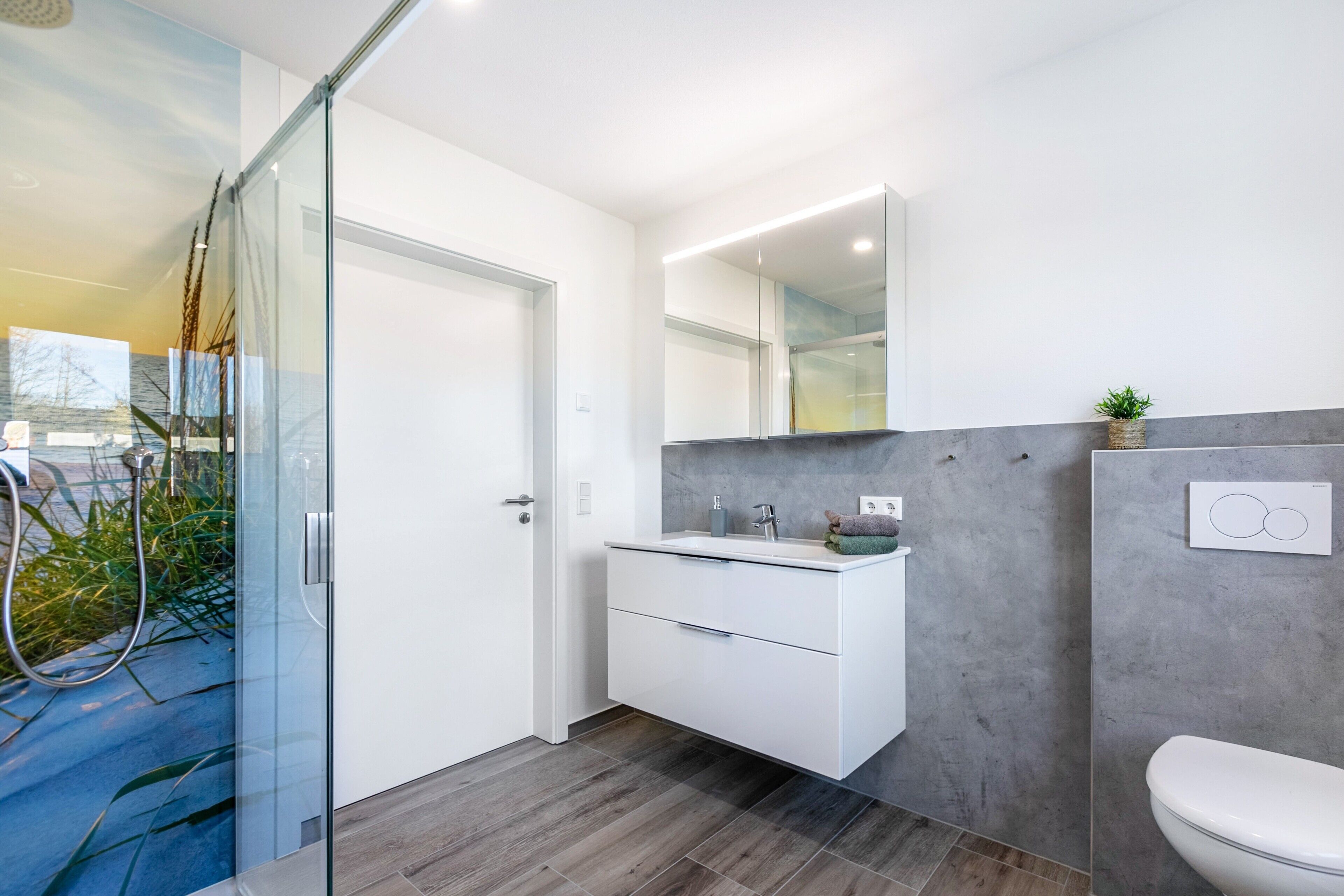 A modern bathroom with a glass shower enclosure, a white sink with a grey countertop, and a white toilet.