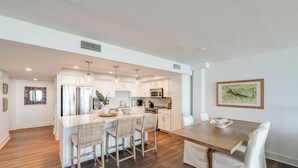 A modern kitchen with white cabinetry, a central island with bar stools, and a dining table with chairs. - Private Balcony With Unforgettable Waterfront Views (Port Aransas)