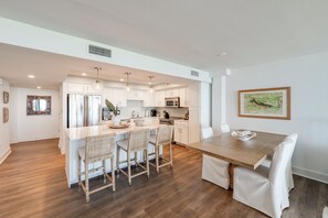 A modern kitchen with white cabinetry, a central island with bar stools, and a dining table with chairs. - Private Balcony With Unforgettable Waterfront Views (Port Aransas)