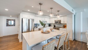 A modern kitchen with white cabinetry, stainless steel appliances, and a central island with bar stools. - Private Balcony With Unforgettable Waterfront Views (Port Aransas)
