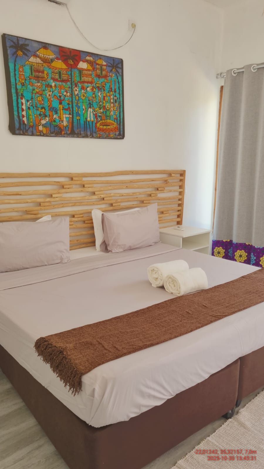 Una cama bien hecha con una manta marrón, un cabecero de madera y un cuadro de colores en la pared.