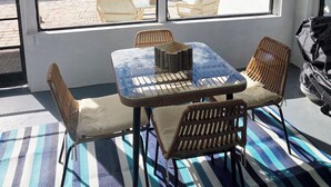 Varanda coberta com mesa e cadeiras, grandes janelas e vista para a água.