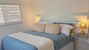 Quarto com cama, mesas de cabeceira, ventilador de teto e janela com persianas.