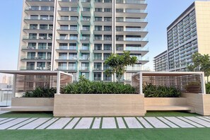 A modern building with multiple balconies and a rooftop garden with planters and artificial grass. - PVH - Serene 1BR - Binghatti House (Dubai)