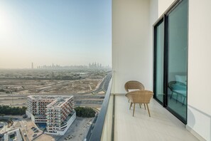 A balcony with wicker chairs and a glass table, overlooking a cityscape with a modern building and roads. - PVH - Serene 1BR - Binghatti House (Dubai)