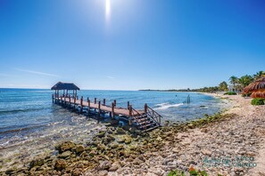 Ein Strand mit einer hölzernen Pier, die zu einem Gebäude mit einem Reetdach führt.