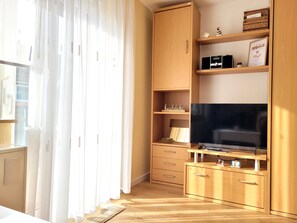 Une chambre moderne avec un meuble en bois, un téléviseur à écran plat et une fenêtre ornée de rideaux légers.