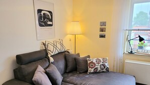 A modern living room with a grey sofa, a lamp, and a window with a view. - Seestern incl. Beach Chair at the Beach (Horumersiel-Schillig)