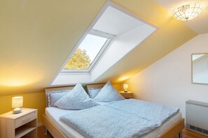 A bedroom with a sloped ceiling, a skylight, a bed with patterned bedding, bedside tables with lamps, and a radiator. - Seestern with a Beach Chair on the Beach (Horumersiel-Schillig)