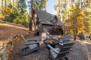 A cabin with a stone wall, a fire pit, and Adirondack chairs. - Campwest Lodge- BLS, A/C (Arnold)