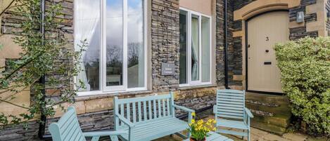 A stone building with a sign reading 'School Cottages.' There are outdoor seating arrangements and a potted plant.