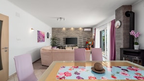 A modern living room with a sofa, a dining table with chairs, a TV, and a fireplace. - Holiday home Silvija by Villas Guide (Primorski Dolac)