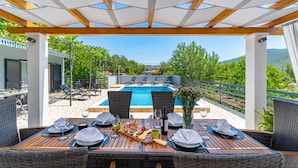 An outdoor dining area with a pool and poolside chairs, overlooking a scenic landscape. - Holiday home Silvija by Villas Guide (Primorski Dolac)