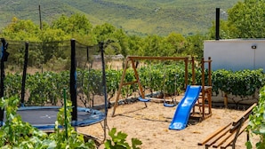 A playground with a trampoline, swing set, and slide, surrounded by grapevines and a mountainous backdrop. - Holiday home Silvija by Villas Guide (Primorski Dolac)